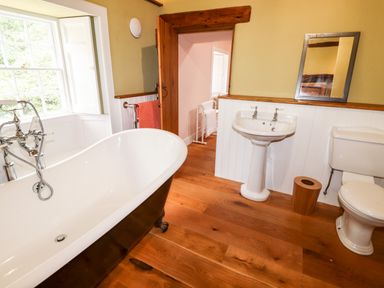 A bathroom with a freestanding bathtub pedestal sink toilet and wooden floor at Eagle Farmhouse in Glenridding