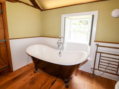 A bathroom with a freestanding bathtub under a window and a towel rail at Eagle Farmhouse in Glenridding