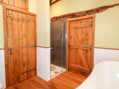 A bathroom with wooden doors a glass shower enclosure and a white bathtub at Eagle Farmhouse in Glenridding