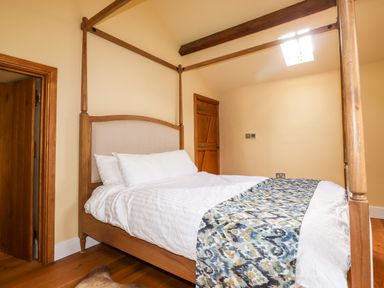 A bedroom with a wooden four-poster bed white bedding and a patterned runner at Eagle Farmhouse in Glenridding