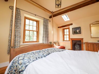 A bedroom with a wooden four-poster bed patterned curtains a small window seat near a fireplace and wooden cabinet at Eagle Farmhouse in Glenridding
