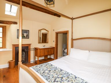 A bedroom with a four poster bed a wooden vanity with sink and a small fireplace at Eagle Farmhouse in Glenridding