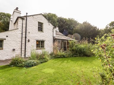 A white stone house with a green lawn and garden plants at Eagle Farmhouse in Glenridding