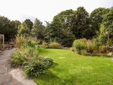 A garden with green grass bordered by plants and trees at Eagle Farmhouse in Glenridding