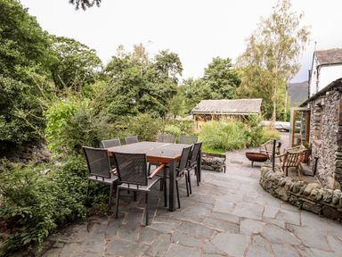 An outdoor patio with a dining table and chairs surrounded by greenery and stone walls at Eagle Farmhouse in Glenridding
