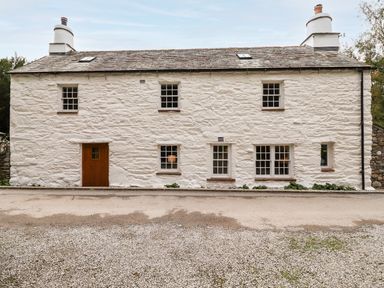The exterior of a two-story white stone house with multiple windows and a wooden door at Eagle Farmhouse in Glenridding