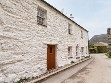 A white stone cottage with brown wooden door and multiple windows along a narrow road at Eagle Farmhouse in Glenridding
