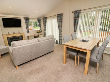 A living room with a grey sofa a wooden dining table with four chairs a fireplace and windows with plaid curtains at The Warren in Hellifield