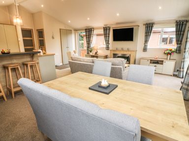A dining table with chairs and a living room with sofas a fireplace and a wall-mounted TV at The Warren in Hellifield