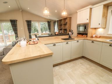A kitchen with wooden countertops white cabinets a microwave a knife set and a teapot with treats on the counter at The Warren in Hellifield
