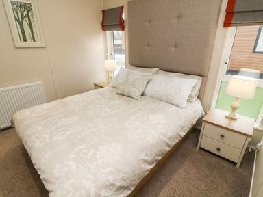 A bedroom with a bed with patterned bedding two bedside tables with lamps and windows at The Warren in Hellifield