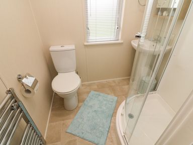 A bathroom with a toilet a shower enclosure a sink a towel radiator and a blue rug on the floor at The Warren in Hellifield