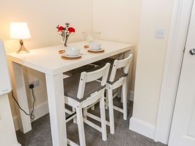 A white dining table with two chairs and tableware next to a wall with a lamp at 24 Baxtergate in Whitby
