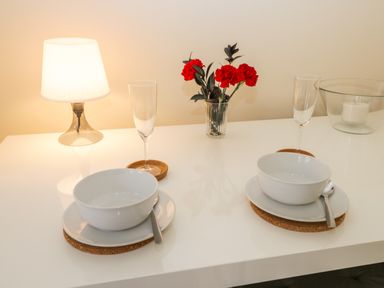A dining table set with two bowls on plates with spoons two glasses a lamp and a vase with red flowers at 24 Baxtergate Whitby