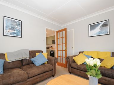 A sitting room with two brown sofas with cushions and a vase of white flowers on a wooden table at Sea Spray in Port Isaac