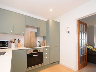 A kitchen with green cabinets a microwave a knife block a toaster and an oven at Sea Spray in Port Isaac