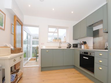 A kitchen with green cabinets wooden floor and a door leading to a conservatory at Sea Spray in Port Isaac
