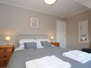 A bedroom with a bed with gray bedding two bedside tables with lamps and a mirror on the wall at Sea Spray in Port Isaac