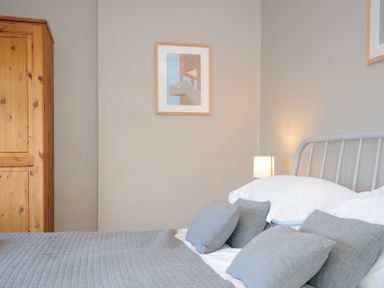 A bedroom with a bed with gray pillows and blanket a wooden wardrobe and a framed picture on the wall at Sea Spray Port Isaac