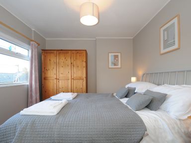 A bedroom with a double bed grey bedding wooden wardrobe and two framed pictures on walls at Sea Spray in Port Isaac