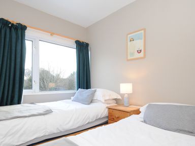 A bedroom with two beds a wooden nightstand lamp and a window with dark curtains at Sea Spray in Port Isaac