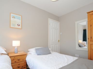 A bedroom with two single beds a wooden nightstand with a lamp a wooden wardrobe a wall mirror and a framed picture at Sea Spray in Port Isaac