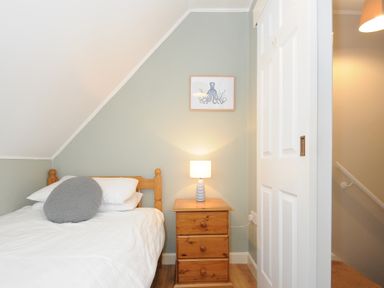 A bedroom with a bed a bedside table with a lamp and an octopus picture on the wall at Sea Spray in Port Isaac