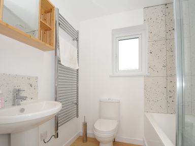 A bathroom with a sink, toilet, bathtub with tiled wall, towel rack, and small window at Sea Spray in Port Isaac