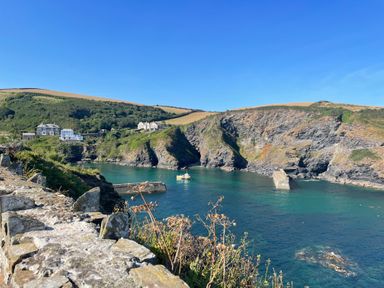 A coastal scene with cliffs a stone wall houses and a boat in the water at Sea Spray in Port Isaac