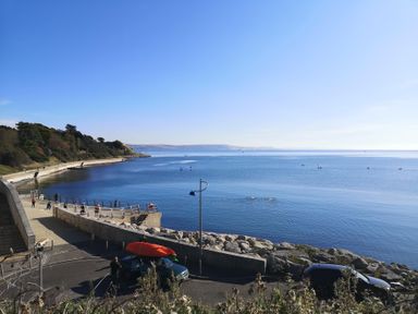 A coastal walkway with people exercising near calm sea and parked cars at Bayview Loft in Weymouth