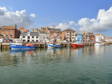 Boats docked along a waterfront with buildings and a pub in the background at Bayview Loft in Weymouth