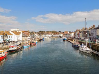 A harbor with boats docked along both sides and buildings lining the waterfront at Bayview Loft in Weymouth