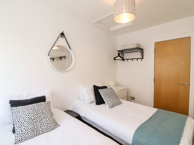 A bedroom with two single beds white bedding black and white pillows a round mirror a wooden door and a wall rack at Bayview Loft in Weymouth