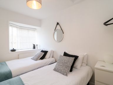A bedroom with two single beds a round mirror above one bed and a window with blinds at Bayview Loft in Weymouth