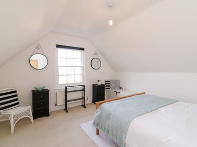 A bedroom with a bed a window two small black drawers two hanging round mirrors and a white chair at Bayview Loft in Weymouth