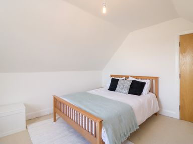 A bedroom with a wooden bed frame white bedding black and white pillows a light blue blanket a white rug and a wooden door at Bayview Loft in Weymouth