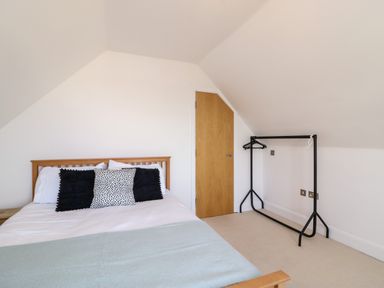 A bedroom with a wooden bed and black and white cushions with a black clothes rack and a wooden door at Bayview Loft in Weymouth