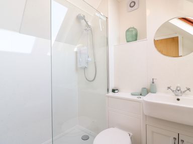 A bathroom with a shower area, a toilet, a sink with a faucet, and a round mirror at Bayview Loft in Weymouth