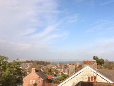 A view of rooftops and chimneys with trees and water in the background at Bayview Loft in Weymouth