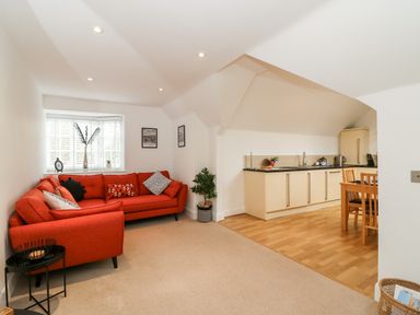A living room with an orange sectional sofa and a small black side table next to a kitchen area with light wood cabinets and dining table at Bayview Loft in Weymouth