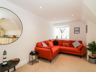 A living room with a red corner sofa and round mirror on the wall at Bayview Loft in Weymouth