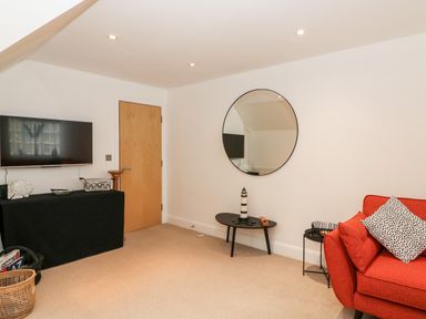 A living room with a red sofa, round mirror on the wall, black table with lighthouse decoration and a TV mounted on the wall at Bayview Loft in Weymouth