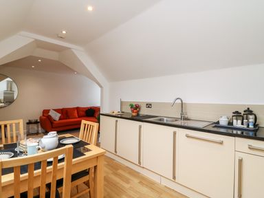 A kitchen and dining area with a wooden dining table and chairs and a red sofa in the background at Bayview Loft in Weymouth