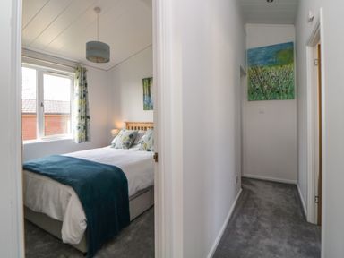A bedroom with a bed and a window beside a hallway with a painting on the wall at Meadow Lodge in Newton Ferrers