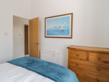 A bedroom with a wooden chest of drawers a radiator a door and a framed picture of a sailboat at Meadow Lodge in Newton Ferrers