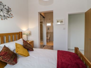 A bedroom with a wooden bed a bedside table with a lamp and an ensuite bathroom at Meadow Lodge in Newton Ferrers