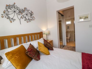 A bedroom with a wooden bed frame and decorative pillows next to a nightstand with a lamp and an ensuite bathroom at Meadow Lodge in Newton Ferrers