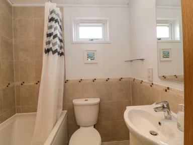 A bathroom with a bathtub and shower curtain a toilet a sink with faucet a small window and a mirror at Meadow Lodge in Newton Ferrers