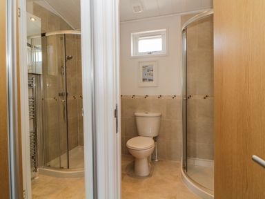 A bathroom with a toilet and a corner shower with glass doors at Meadow Lodge in Newton Ferrers