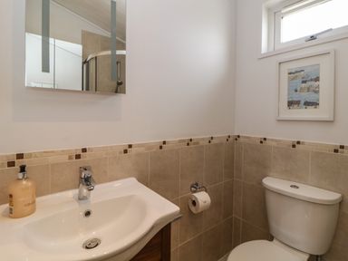 A bathroom with a sink soap dispenser toilet paper holder toilet and a framed picture on the wall at Meadow Lodge in Newton Ferrers